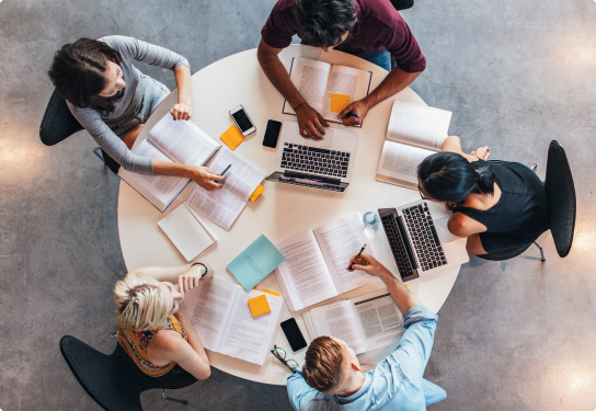 Case Study - Manukau Institute of Technology - Image Image of students sitting around a round table with laptops, books, phones an documents studying