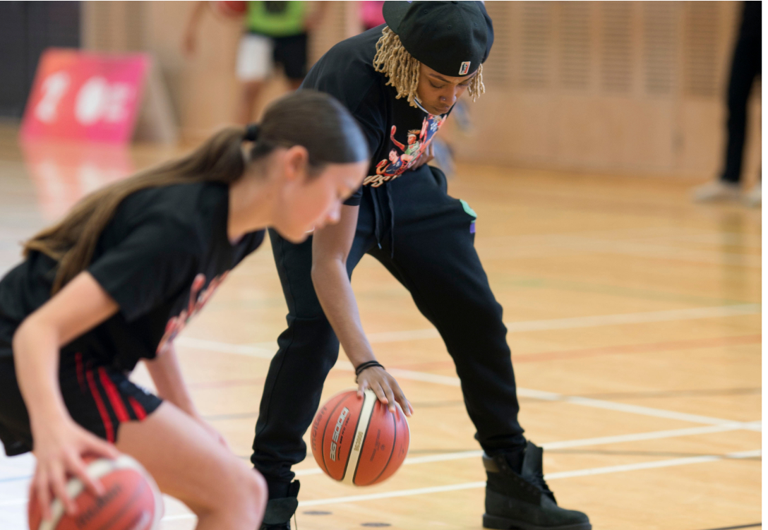 Photo of a basketball coach showing a girl how to dribble the basketball