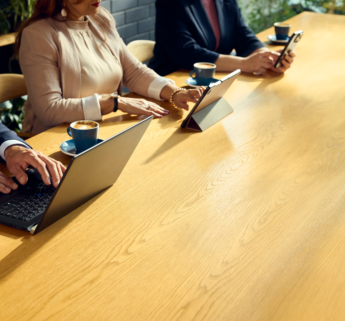 People sitting at a desk on laptops and phones drinking coffee